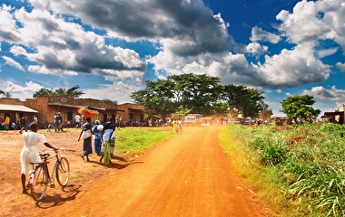 Women walking and pushing bicycles by the side of a dirt road in rural Africa