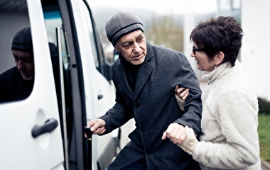 Woman helping an older man into a transit vehicle