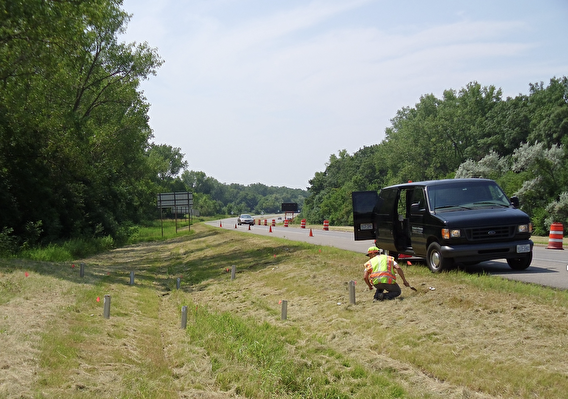 A researcher crouching in a swale on the side of a roadway