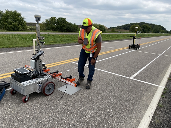 Worker in a safety vest examining the pavement testing automated robot