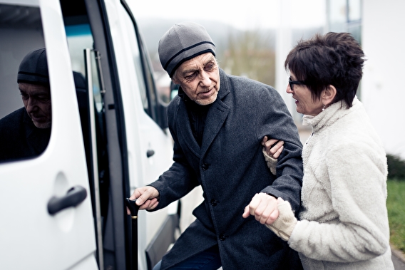 A woman helping an older man using a cane into a vehicle